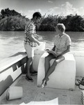 Technician De Campbell, (seated in photograph), takes notes for graduate student Bruce Burgener as he collects water samples for a nutrient pollution study